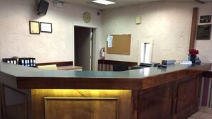 A reception desk with a wooden counter, a clock, framed certificates, and a bulletin board. - Magnuson Hotel Columbia (Columbia)