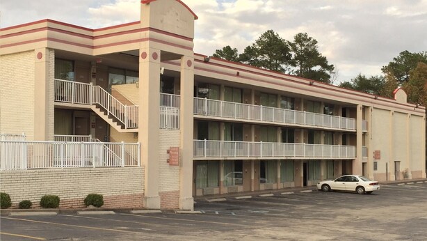 A multi-story motel with balconies, a parking lot, and a white car parked in front. - Magnuson Hotel Columbia (Columbia)