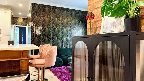 En modern inredning med en bardisk, en vägg med ett mönster, en grön soffa och ett skåp med en unik design.