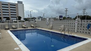 Ein rechteckiger Swimmingpool mit weißem Rand, umgeben von einem weißen Zaun mit Stühlen.