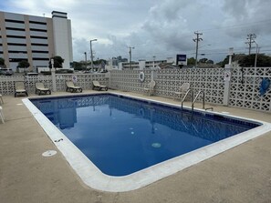A rectangular swimming pool with a white border, surrounded by a white fence with chairs. - Travelodge by Wyndham Virginia Beach (Virginia Beach)