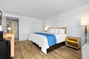 A hotel room with a bed, bedside table, lamp, desk, chair, and a washing machine. - Travelodge by Wyndham Virginia Beach (Virginia Beach)