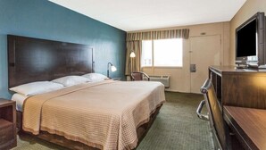 Ein Hotelzimmer mit einem großen Bett, einem Schreibtisch, einem Sessel, einem Fernseher und einem Fenster mit Vorhängen.