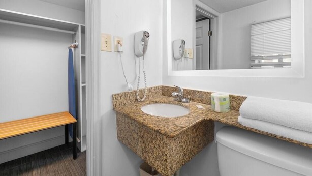 A bathroom with a granite sink, a mirror, a bench, and a toilet. - Travelodge by Wyndham Virginia Beach (Virginia Beach)