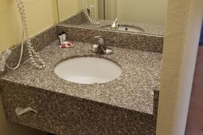 Un baño con encimera de granito, un lavamanos blanco, un espejo y un perchero para toallas.
