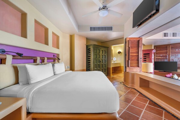 A hotel room with a bed, a television, a ceiling fan, and a bathroom visible through an open door.
