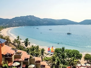 Vista costera con playa, veleros y palmeras.