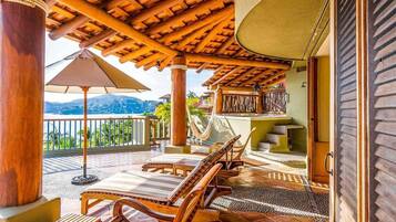 Una terraza de madera con sillones de descanso y una hamaca, con vistas a un paisaje montañoso.