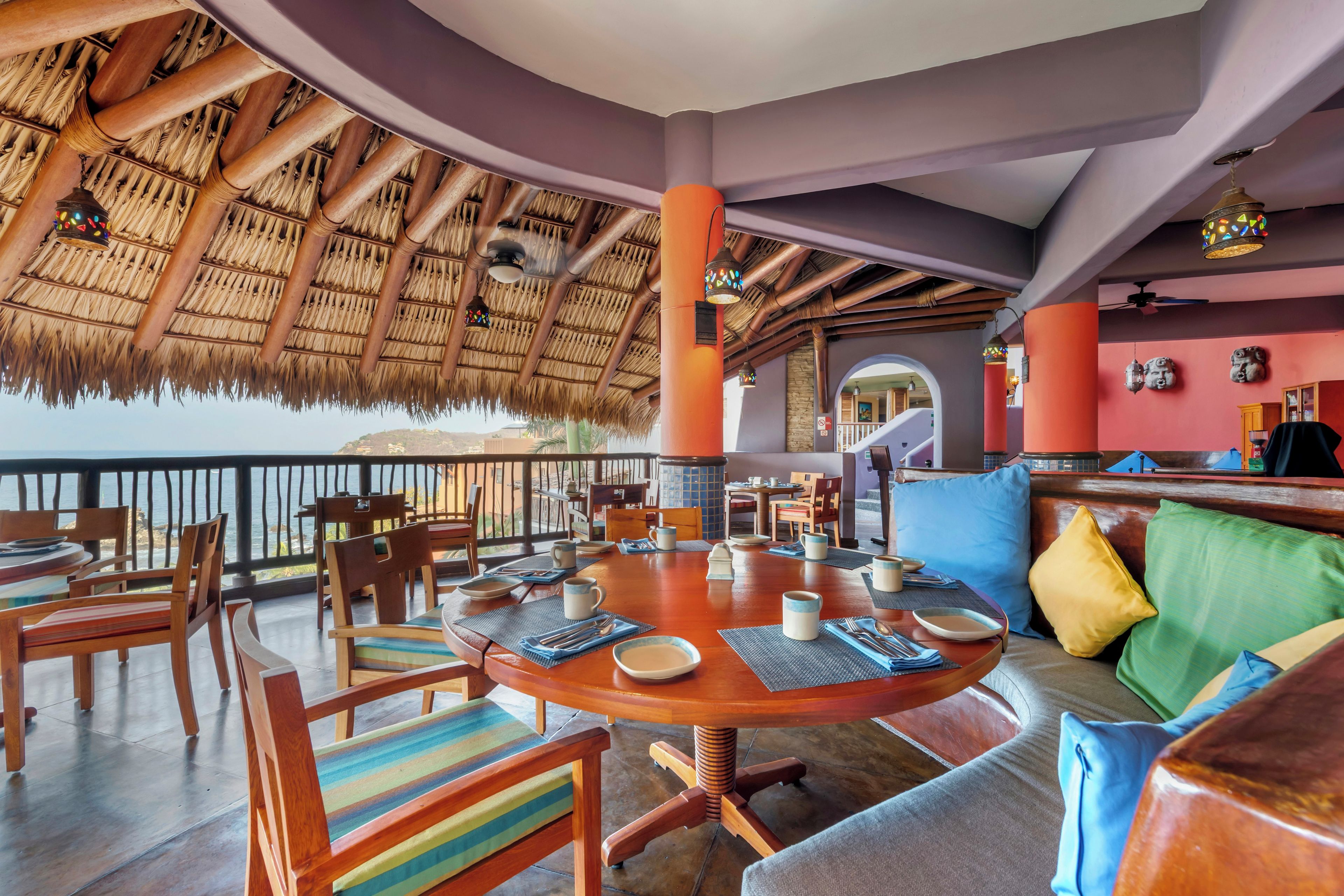 Restaurante com telhado de palha, móveis de madeira e vista para o mar.