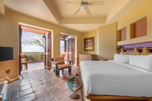 A hotel room with a bed, a television, a desk, and a chair. There is a balcony with a view of palm trees. - Hilton Grand Vacations Club Zihuatanejo (Zihuatanejo)