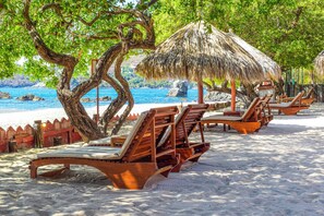 Een strand met houten ligbedden en rieten parasols.