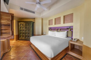 Una habitación de hotel con cama, armario de madera, ventilador de techo y piso de baldosas.