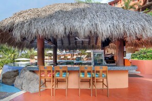 Eine Bar mit einem Strohdach, einem Außenpool und Liegestühlen.