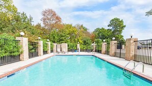 A rectangular swimming pool with a brick border, surrounded by a stone wall and metal fencing. - Baymont by Wyndham Tyler (Tyler)