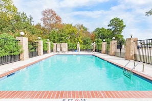 Una piscina rectangular con borde de ladrillo, rodeada por un muro de piedra y una valla de metal.