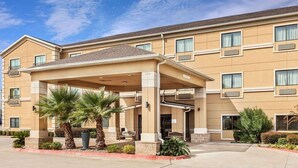 A multi-story hotel with a covered entrance, palm trees, and a clear sky. - Baymont by Wyndham Tyler (Tyler)