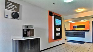 A hotel reception area with a coffee machine, a digital screen, and a sign offering free morning coffee.