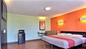 A hotel room with a bed, a desk with a chair, a microwave, and a refrigerator.