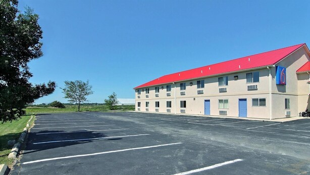 A multi-story building with a red roof, a parking lot with marked spaces, and a clear blue sky.