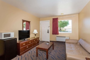 A hotel room with a television, a small refrigerator, a wooden dresser, a sofa, a table, and a window with curtains. - Super 8 by Wyndham Hurricane Zion National Park (Hurricane)