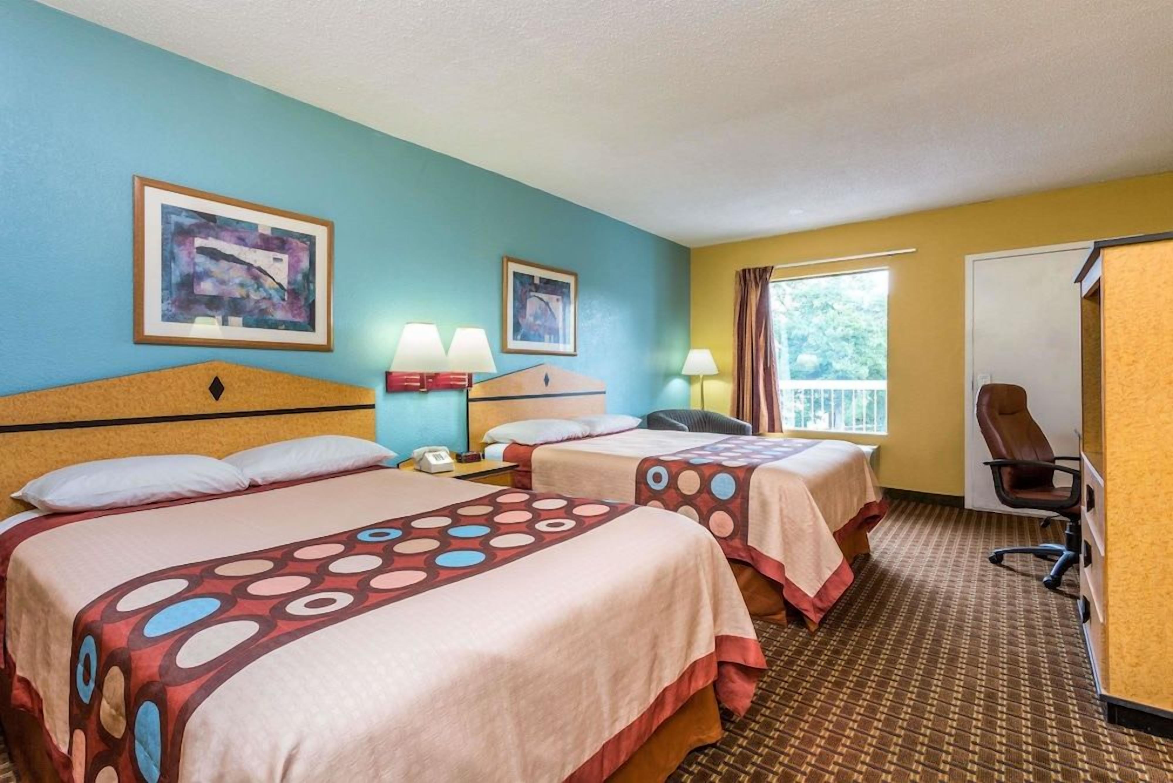 A hotel room with two beds, a desk, a chair, and a window with curtains.