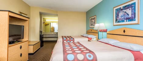 Habitación de hotel con dos camas, televisión, escritorio y baño visible a través de una puerta abierta.