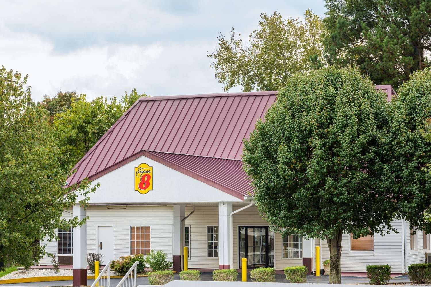 A building with a red roof and a Super 8 logo, surrounded by trees and shrubs.