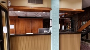 A reception area with a wooden counter, a blue pillar, and a staircase in the background.
