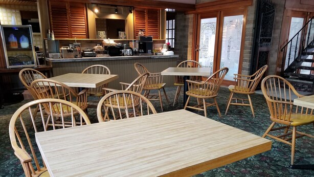 A restaurant interior with wooden tables and chairs, a bar area, and a staircase.