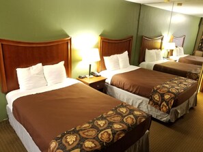 A hotel room with three single beds, each with a wooden headboard, white bedding, and a patterned throw. There is a nightstand with a lamp and a telephone on each bed. - Raintree Inn (Ada)
