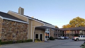A building with a stone facade, a covered entrance, and a parking lot with several cars.