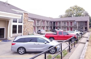 A parking lot with several cars, a red truck, and a building with multiple balconies and windows. - Raintree Inn (Ada)