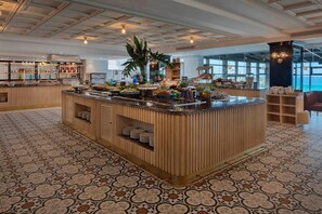 A buffet area with a central island, a tiled floor, and a view of the sea through large windows. - Resort Hadera by Jacob Hotels (Hadera)