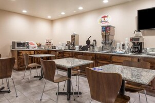 Un área de desayuno con mesas, sillas, una máquina de café, un microondas y un letrero para un restaurante de desayunos.