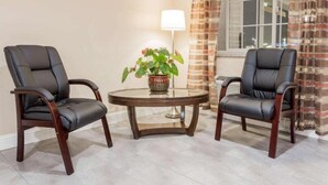 Dos sillones de cuero, una mesa redonda y una planta en maceta en una habitación con ventana y cortinas a rayas.