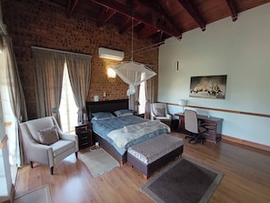 A bedroom with a bed, a chair, a desk, a lamp, a painting, and a brick wall.