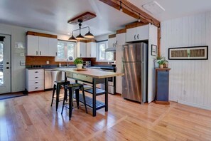 A modern kitchen with wooden floors, a central island, stainless steel appliances, and pendant lighting.