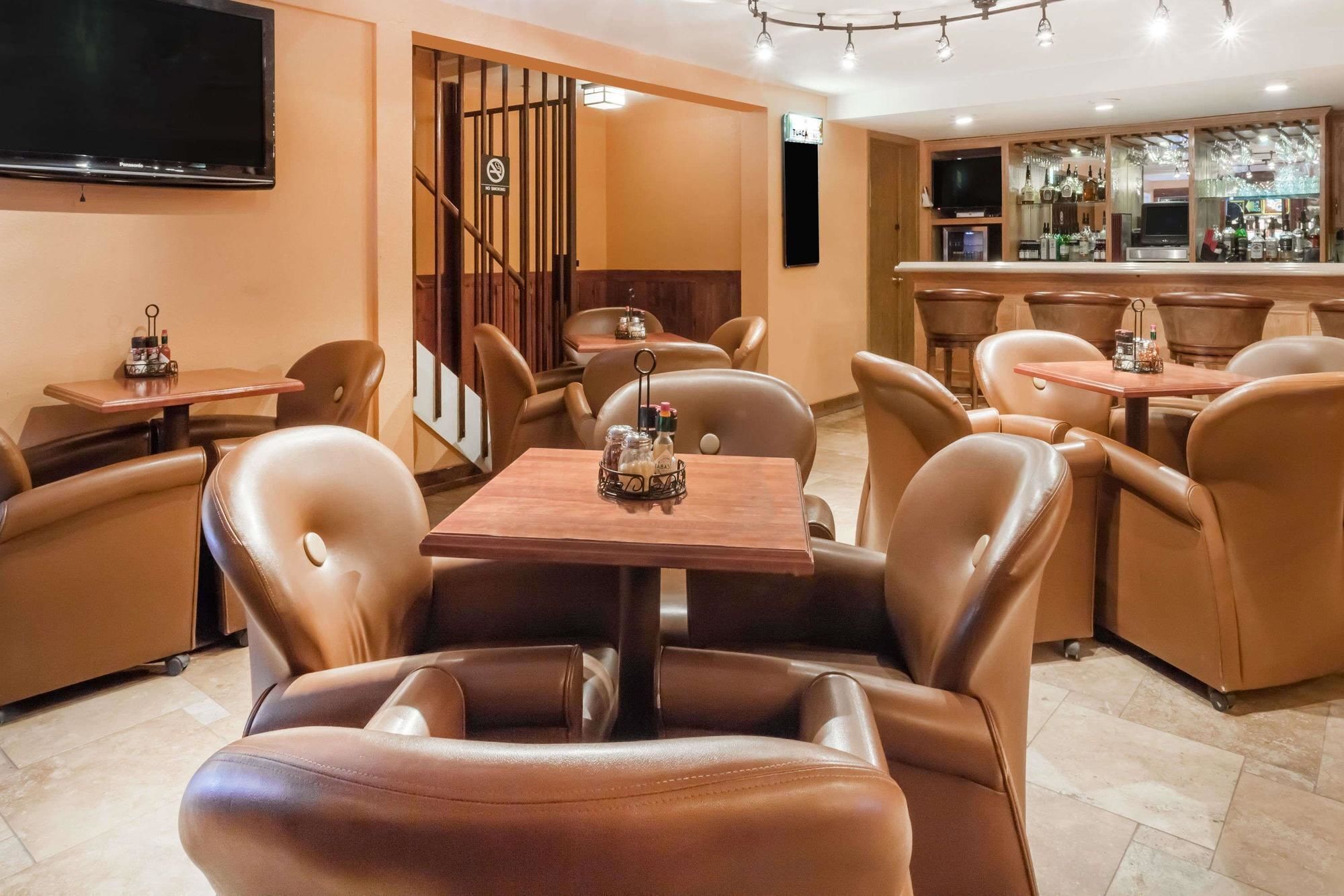 A restaurant with leather chairs, wooden tables, a bar area, and a TV mounted on the wall.