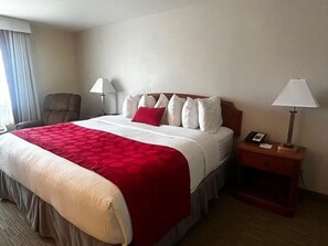A hotel room with a bed, two bedside lamps, a chair, a nightstand, and a window with curtains.