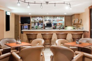 A bar area with leather chairs, a television, and a bar stocked with bottles.
