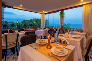 A restaurant with tables set for dining, a view of the sea, and a balcony with plants. - Harmony Istanbul (Istanbul)