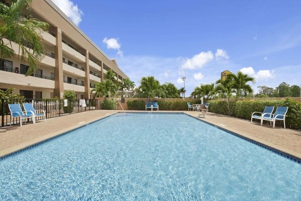 A swimming pool with lounge chairs, a multi-story building, and palm trees. - Super 8 Fort Myers Hotel (Fort Myers)