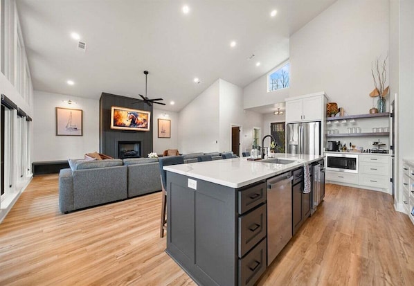 A modern kitchen with a large island, white cabinetry, and a dining area with a grey sofa. - Private Pool, Dock, Movie Room on Lake Hamilton (Hot Springs)