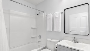 A bathroom with a bathtub, toilet, sink, and a mirror. - Suburban Studios Lakeland North I-4 (Lakeland)