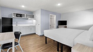 A compact room with a bed, a small kitchenette, a TV, and a chair. - Suburban Studios Lakeland North I-4 (Lakeland)