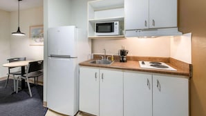 A compact kitchen with white cabinets, a microwave, a sink, and a stove. There is a chair and a table in the adjacent dining area. - Suburban Studios Lakeland North I-4 (Lakeland)