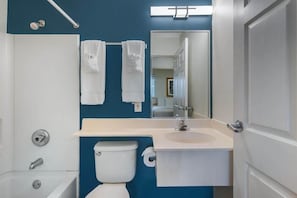 Un baño con inodoro, lavabo y bañera. Hay toallas colgadas en la pared y un espejo sobre el lavabo.