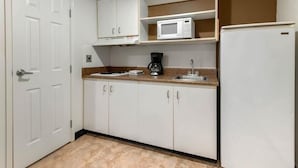 Una cocina compacta con armarios blancos, microondas, cafetera y refrigerador.
