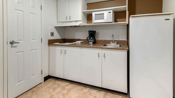 A compact kitchen with white cabinets, a microwave, a coffee maker, and a refrigerator. - Suburban Studios Lakeland North I-4 (Lakeland)