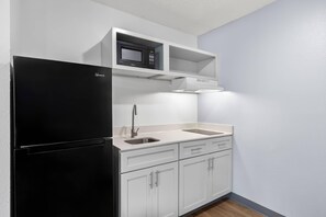 Una cocina compacta con un refrigerador negro, un microondas y un lavabo.